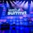 A large stage setup with an illuminated sign reading 'Web Summit' against a backdrop of stacked cube-like structures with purple and blue lighting. Several spotlights shine from above, and there is a seating arrangement that includes chairs and a table.